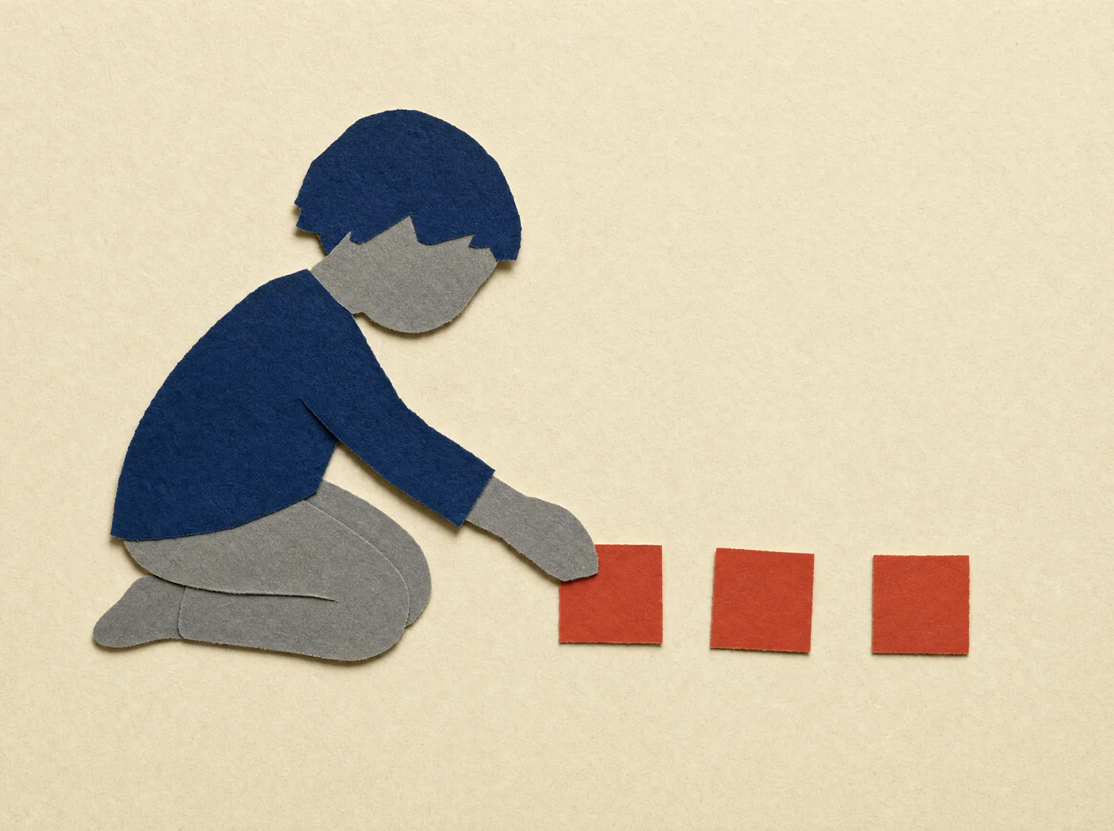 A paper child lays three small red paper squares in a row.